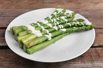 Appetizing asparagus in sour cream sauce on white plate against wooden background