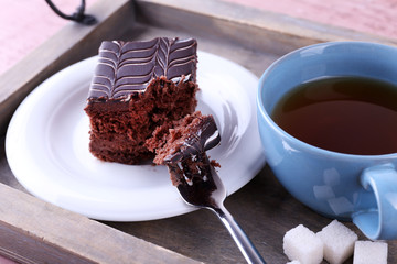 Served table with a cup of tea and chocolate cake on wooden background close-up