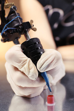 Tattoo machine in hand with red paint on the table, close up