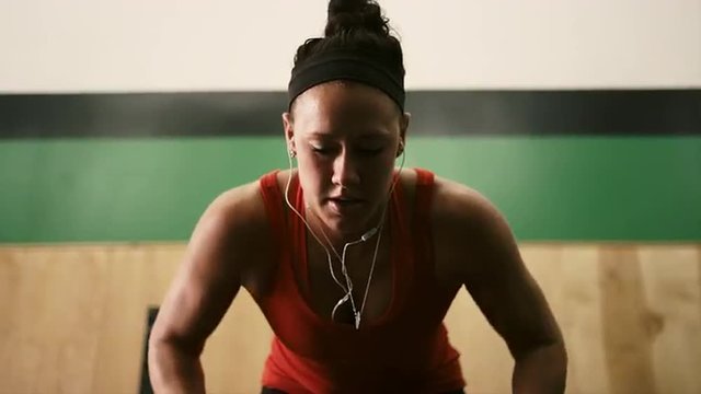 Close up of a fit young woman lifting dumbbells and listening to music in a small gym