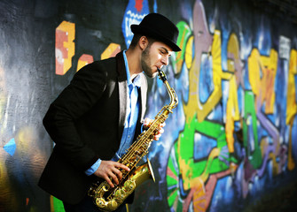 Young man with saxophone outside near the old painted wall