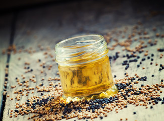 Oil of mustard in a small jar and yellow and black mustard seeds
