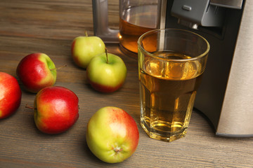 Stainless juice extractor with apples and glass of juice on wooden background, close up