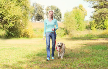 Naklejka na ściany i meble happy owner woman and Golden Retriever dog walking together in s