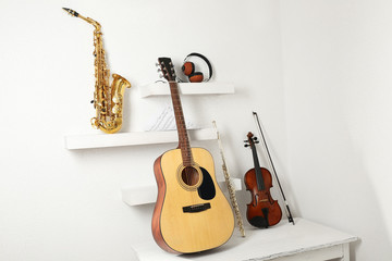 Musical instruments and headphones on decorated shelves against white wall background