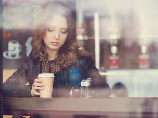 Young woman drinking coffee sitting indoor in urban cafe. Cafe city lifestyle. Casual portrait of teenager girl. Toned