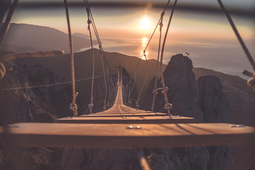 Rope ladder over abyss leading to a catholic cross during sunrise 