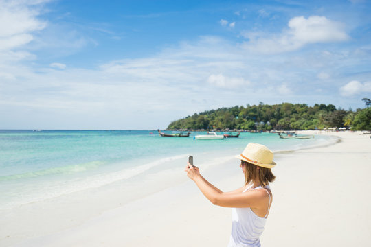 Female tourist taking photo of beautiful beach on smartphone.