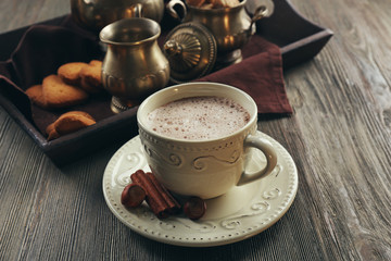 Vintage cup of cacao on wooden table against tray with silver service and cookies