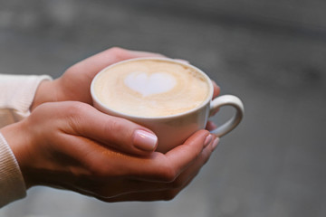 Cup of cappuccino in hands on blurred background