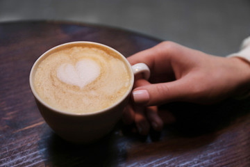 Cup of cappuccino in hand on blurred background
