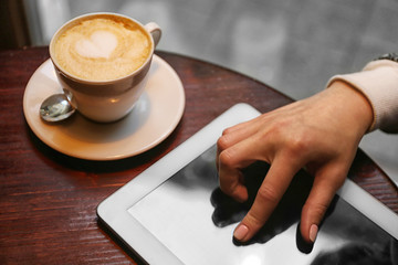 Girl hand with digital tablet and cappuccino on a wooden table