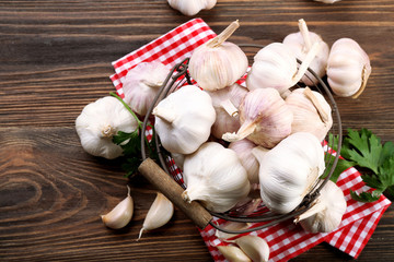Fresh garlic in the basket decorated with parsley and red checkered cotton napkin on wooden background