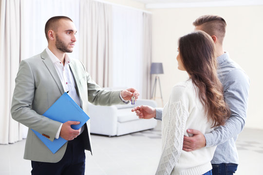 Estate agent giving keys to  couple, on light background
