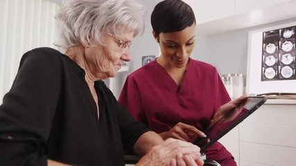 Elderly white woman and young black nurse looking at a tablet