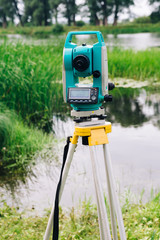 blue surveying equipment total station on a background of lake and forest