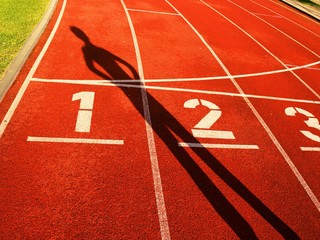 Athlete dark sharp body shadow on a red running track in stadium
