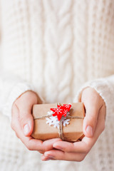Woman in knitted sweater holding a present. Gift is packed in craft paper with red fir tree.