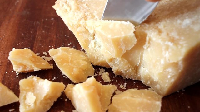 cutting pieces of parmesan cheese with a knife on a wooden chopping board