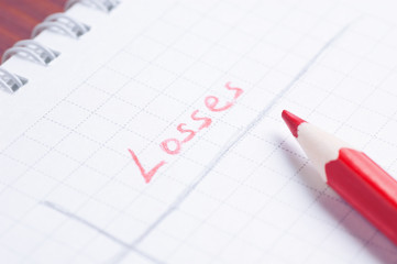 Notepad with handwritten word Losses by red pencil lying over paper sheet cold filtered shallow depth of field