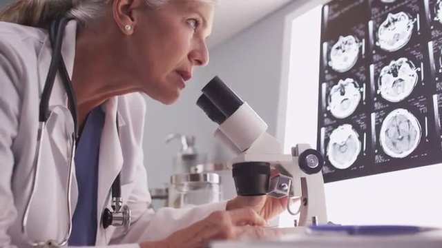 Middle aged neurologist female researching with microscope