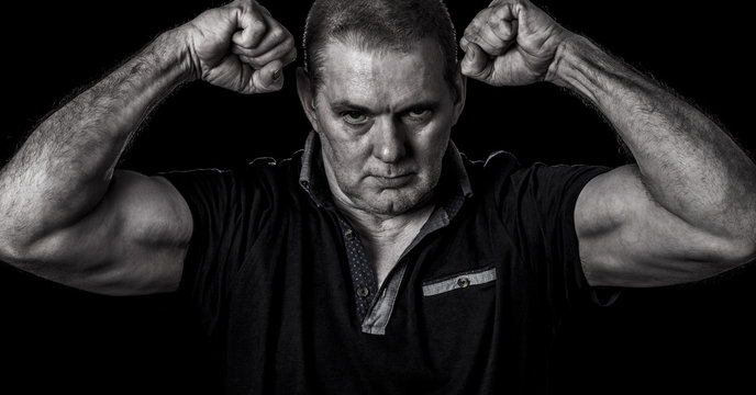 Gritty Image Of An Unshaven Guy Posing With Clenched Fists And His Biceps Flexed On A Black Background