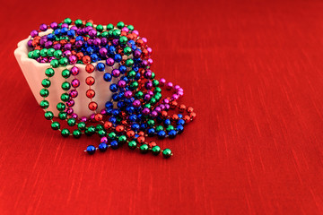 Holiday beads flowing out of a white bowl onto a red tablecloth
