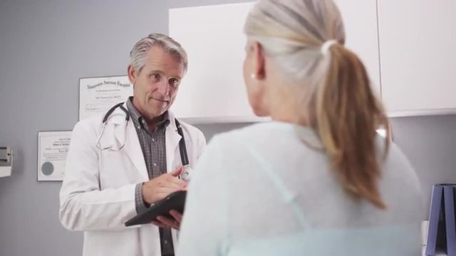 Mid-aged medical doctor consulting a patient with tablet