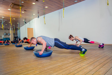 People at the health club with personal trainer, learning correct form. bosu