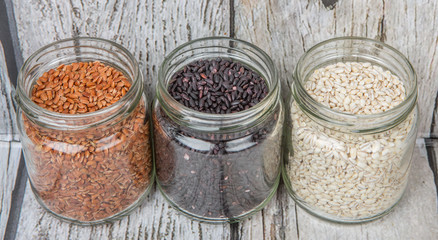 White, brown, black millet in mason jars over wooden background