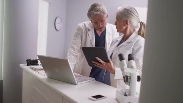 Two senior medical doctors looking at a tablet and laptop computer