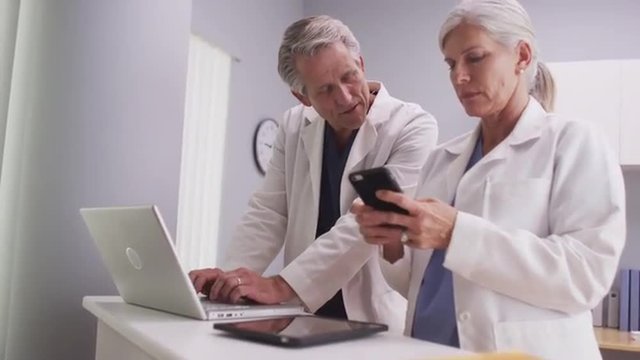 Senior female doctor with male colleague looking at cell phone  
