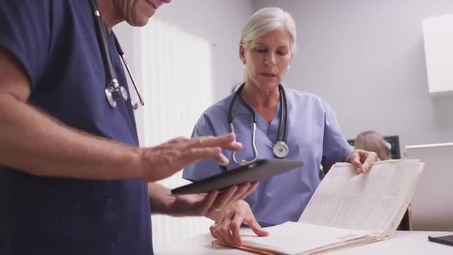 Senior Female Medical Doctor Or Nurse Reading Patient File With Male Colleague