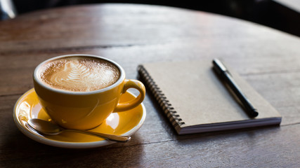 Hot latte art coffee cup on wooden table and note book.