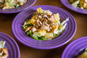 Fresh salad with chicken meat, oranges, walnuts, greens and herbs and olive oil on a bright colorful ceramic plates. Portion of salad on the background of cardboard with space for your text or menu.