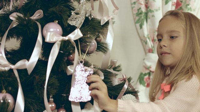 Beautiful blue-eyed girl hangs a homemade Christmas toy on Christmas tree