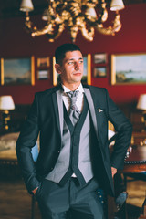 Fototapeta premium Happy groom in luxury chairs in chic interiors of wedding palace