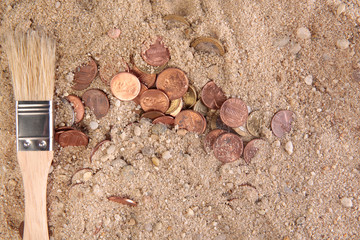 coins in the sand with brush