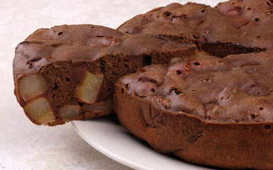Homemade chocolate cake with pieces of pears on a white plate. 