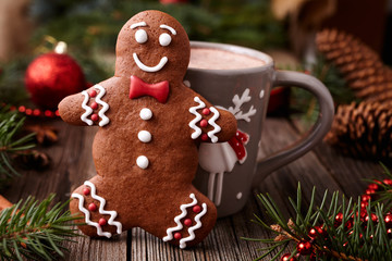 Cup of hot chocolate or cocoa beverage with cinnamon and gingerbread man cookie in new year tree decorations frame on vintage wooden table background. Homemade traditional celebration dessert recipe.