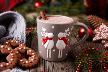 Cup of hot chocolate or cocoa beverage with two cute deer, cinnamon and gingerbread round christmas cookies in new year tree decorations frame on vintage wooden table background.