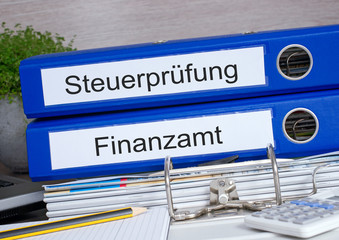 Steuerprüfung und Finanzamt - zwei blaue Ordner mit Taschenrechner und Unterlagen im Büro