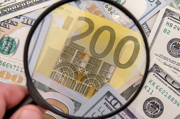 Magnifying glass over 200 euro notes. US dollar in the background