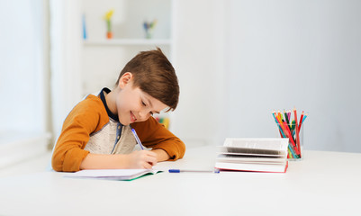 smiling student boy writing to notebook at home - Powered by Adobe