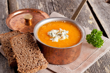pumpkin soup with blue cheese in a copper pot on a wooden table