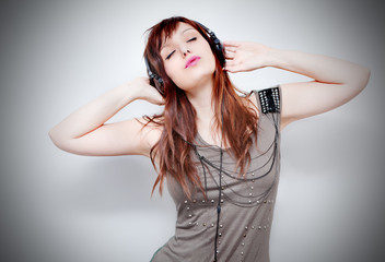 Mujer joven escuchando música con auriculares en fondo neutro. Estilo de vida