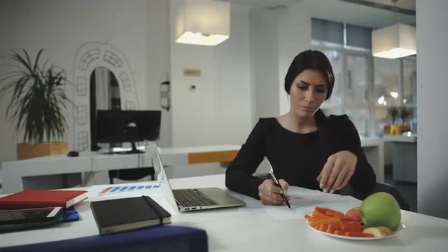 Woman working and eating slices of carrots and apples.