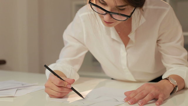 Female fashion designer drawing sketches for clothes in atelier. Happy young fashion designer working in workshop