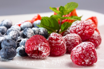 Ягоды посыпанные сахарной пудрой на тарелке.

