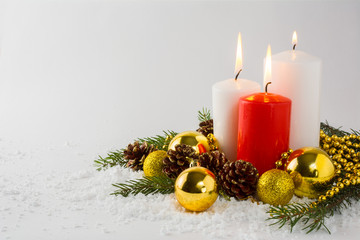Burning white and red Christmas candles, golden balls, fir branches and cones in snow on a white background